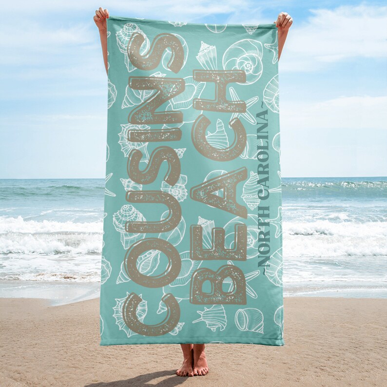 May include: A turquoise beach towel with a white seashell pattern and the text "COUSINS BEACH - NORTH CAROLINA" in brown lettering.
