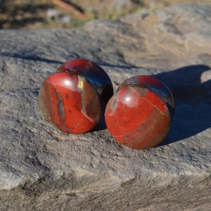 May include: Pair of red, brown, and black stone ear gauges. The gauges are round and have a smooth, polished finish.