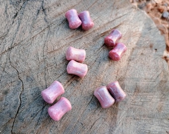 May include: Pink stone ear plugs, cylindrical in shape, are scattered on a weathered wooden surface. The plugs have a smooth, polished finish and a natural, marbled appearance. The plugs are approximately 0.5 inches in length.