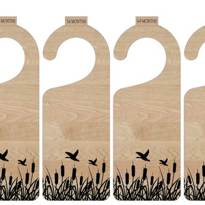 May include: Set of six wooden door hangers with a rustic brown finish. Each hanger features a black silhouette of a bird flying over a field of reeds. The hangers are labeled with the text "14 Months".