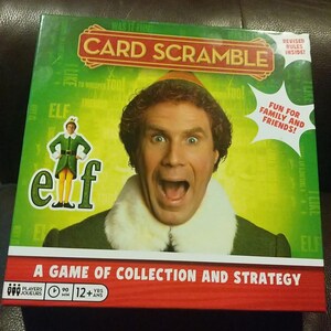 May include: Card Scramble board game box featuring Will Ferrell from the movie Elf. The box has a green background with the word "Elf" in large letters. The game is advertised as fun for family and friends.