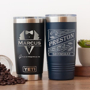 May include: Two personalized stainless steel tumblers with lids. The tumbler on the left is black with the text "Marcus Groomman YETI" and a tuxedo graphic. The tumbler on the right is navy blue with the text "Preston Groomman" in a decorative frame.