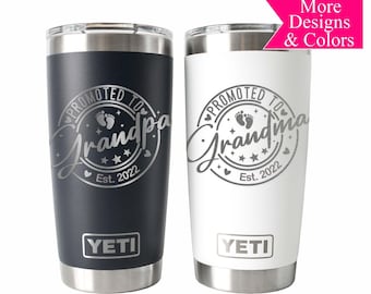 May include: Two stainless steel YETI tumblers with a white and black design. The tumblers are engraved with the text "Promoted to Grandpa" and "Promoted to Grandma" with a footprint graphic and the year 2022.