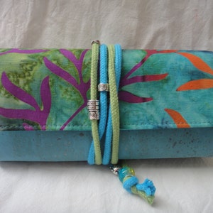 May include: A blue and green fabric clutch with a cork bottom and a turquoise and green cord with silver beads.