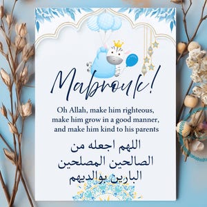 May include: A greeting card with the word "Mabrouk!" in cursive script. The card features a blue and white design with a cartoon zebra holding balloons. The card includes text in English and Arabic.