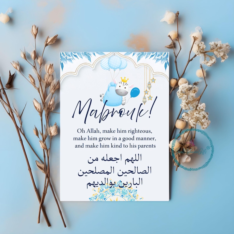 May include: A greeting card with the word "Mabrouk!" in cursive script. The card features a blue and white design with a cartoon zebra holding balloons. The card includes text in English and Arabic.