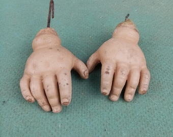 Puede incluir: Dos manos de muñeca vintage hechas de yeso pintado con ganchos metálicos unidos a las muñecas. Las manos son de color piel claro y tienen cinco dedos cada una.