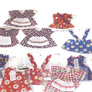 Pode incluir: Uma coleção de vestidos de boneca com vários padrões, incluindo bolinhas, xadrez vichy e estampas florais. Os vestidos apresentam detalhes como aventais, acabamentos em renda e suspensórios. A paleta de cores inclui vermelho, azul e branco.