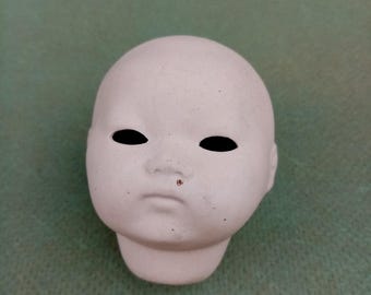 May include: A white porcelain doll head with black painted eyes and a small, slightly upturned nose. The head is unpainted and ready for customization.