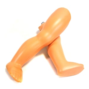 May include: A pair of vintage doll legs in a light peach color, crossed at the ankles. The legs are made of a smooth plastic material and are set against a white background.