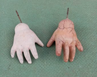 Puede incluir: Dos manos de muñeca vintage hechas de yeso pintado. Una mano es blanca con un tono rosa claro y la otra es marrón claro con grietas en la pintura.