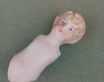 May include: A porcelain doll head with painted blue eyes and a red mouth. The doll has blonde hair and a white torso.