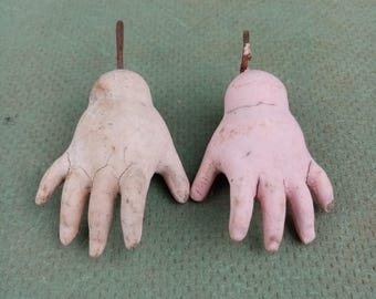 Puede incluir: Dos manos de muñeca vintage hechas de yeso pintado. Una mano es de color rosa pálido y la otra es de color beige claro. Ambas manos tienen cinco dedos y están unidas a un alambre de metal.