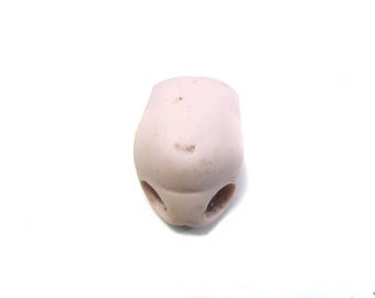 May include: A small, antique doll head fragment. The porcelain head is a pale pink color with three holes at the bottom and a small indentation for the nose. The doll head is set against a white background.