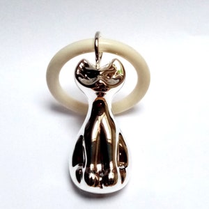 May include: A silver cat figurine with a white ring around its neck. The cat is sitting with its paws tucked under its body.