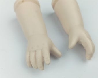 Może przedstawiać: Dwa antyczne ramiona porcelanowej lalki, o jasnym odcieniu skóry. Ramiona są zgięte w łokciu, z palcami lekko zakrzywionymi. Ramiona są prawdopodobnie częściami zamiennymi do zabytkowej lalki.