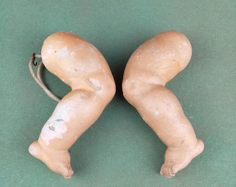 Puede incluir: Dos piernas de muñeca antiguas hechas de yeso pintado. Las piernas están dobladas en la rodilla y tienen los dedos de los pies pintados. Las piernas están atadas a una cuerda.