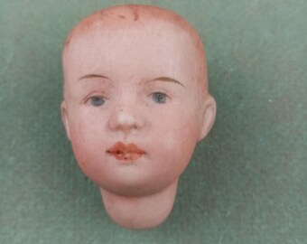 May include: A porcelain doll head with painted blue eyes, a pink mouth, and a light pink complexion.