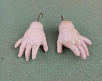 Puede incluir: Dos manos de muñeca de porcelana con enganches de alambre. Las manos son de color rosa pálido y tienen cinco dedos cada una.