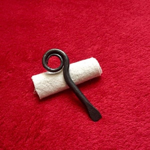 May include: A black metal bottle opener with a curled handle. The opener is resting on a white fabric roll.