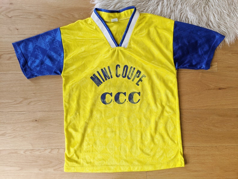 May include: Yellow and blue soccer jersey with the text "MINI COUPE CCC" printed on the front.