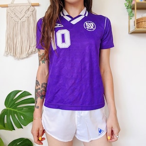 Peut inclure: Un maillot de football violet avec des accents blancs et le numéro 10 sur le devant. Le maillot a un col blanc et un logo blanc avec le texte "AMERICAN YOUTH SOCCER ORGANIZATION" et "FOUNDED 1982".