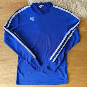 May include: A royal blue long-sleeved shirt with white stripes down the sleeves. The shirt has a mock neck and a small white logo on the chest.