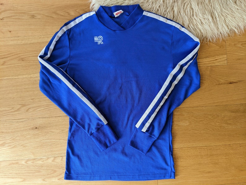 May include: A royal blue long-sleeved shirt with white stripes down the sleeves. The shirt has a mock neck and a small white logo on the chest.