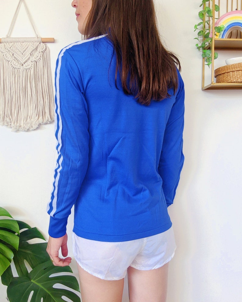 May include: A royal blue long-sleeved shirt with white stripes down the sleeves. The shirt has a high neckline and a relaxed fit.