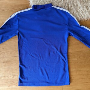 May include: A long-sleeved blue shirt with white stripes down the sleeves. The shirt has a high neck.