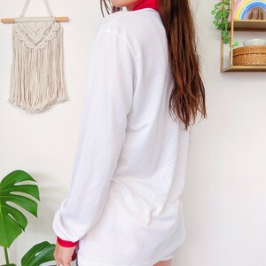 May include: White long-sleeve shirt with a red collar and red trim on the cuffs. The shirt is made of a soft, lightweight fabric.