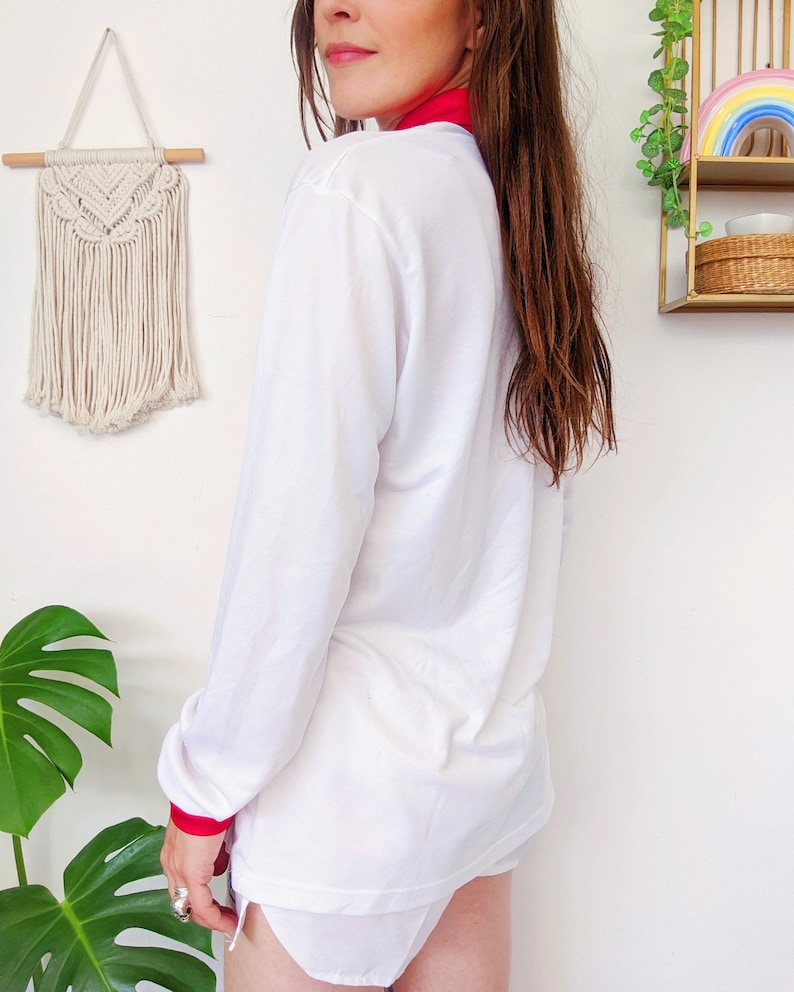 May include: White long-sleeve shirt with a red collar and red trim on the cuffs. The shirt is made of a soft, lightweight fabric.