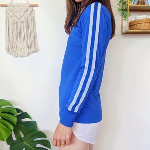 May include: A long-sleeved shirt in a bright blue color with white stripes on the sleeves. The shirt has a crew neck and a relaxed fit.
