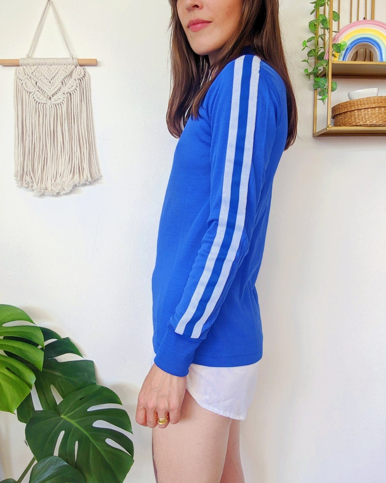 May include: A long-sleeved shirt in a bright blue color with white stripes on the sleeves. The shirt has a crew neck and a relaxed fit.