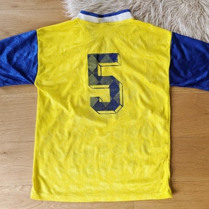 May include: Yellow and blue soccer jersey with the number 5 on the back. The jersey has a diamond pattern on the back.