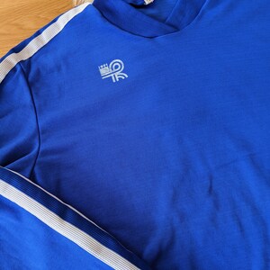 May include: A royal blue long-sleeve shirt with white stripes down the sleeves and a white logo on the left chest that says "LOUI" with a stylized "R" inside a circle.