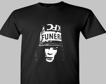 May include: Black t-shirt with a white graphic of a person wearing a helmet with the text "KFC FUNERAL". The design is a bold, stark contrast against the dark fabric. The shirt has short sleeves and a crew neck.