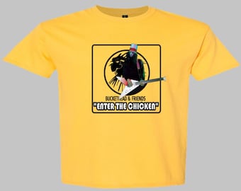 May include: Yellow t-shirt featuring a graphic of a black figure with a guitar, wearing a hat, and the text "ENTER THE CHICKEN". The graphic is inside a black square with a yellow background. The text "BUCKETHEAD & FRIENDS" is above the square.