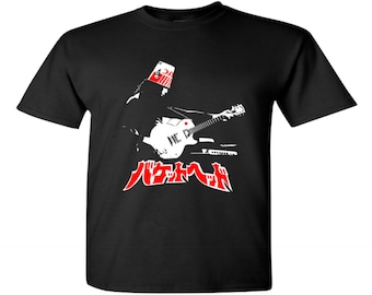 May include: Black t-shirt featuring a graphic of a guitarist wearing a KFC bucket on his head, playing a white guitar. The design includes red Japanese text and a white guitar. The shirt is a classic crew neck.