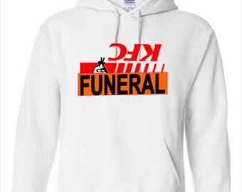 May include: White hooded sweatshirt with a graphic design. The design features the word "FUNERAL" in orange block letters, with the letters "KFC" in red above it. A cartoon image of a chicken is in the design.