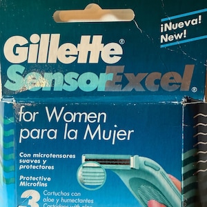 May include: A teal and blue Gillette SensorExcel razor cartridge box. The box reads "for Women" and "Made in U.S.A." The box features a picture of a teal razor and the text "Protective Microfins".