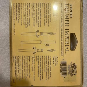 May include: A gold Sheaffer Triumph Imperial fountain pen with a chrome finish and green accents. The pen features a classic design with a stainless steel inlaid nib, a spring-loaded clip, and a refillable ink cartridge system. The packaging includes a pen case.