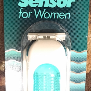 May include: A white and blue razor with the text "Gillette Sensor for Women" on the packaging. The razor has a blue, translucent, replaceable cartridge with two blades.