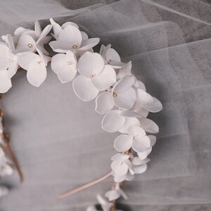 May include: A white floral crown with gold accents. The crown is made of delicate white flowers and is perfect for a wedding or special occasion.