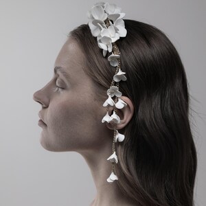 May include: A white floral headband with a delicate gold chain and white flower accents hanging down the side.