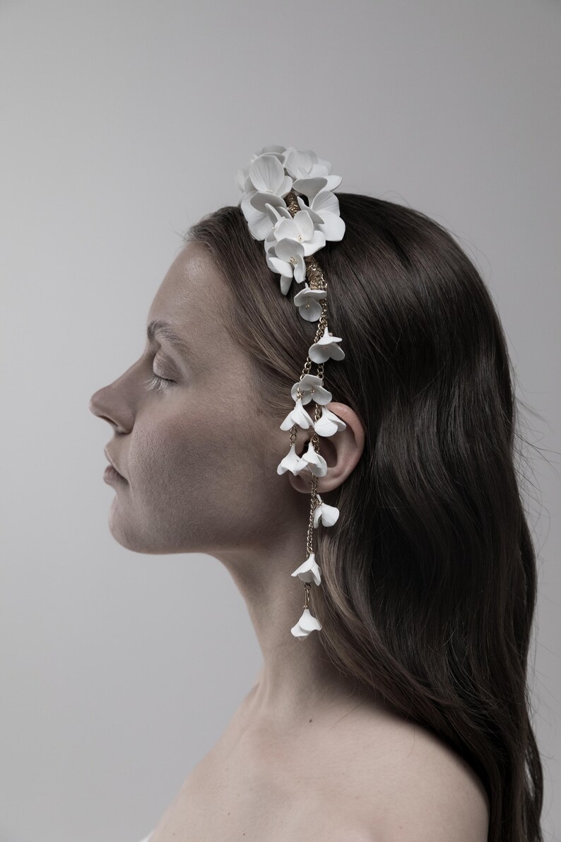 May include: A white floral headband with a delicate gold chain and white flower accents hanging down the side.