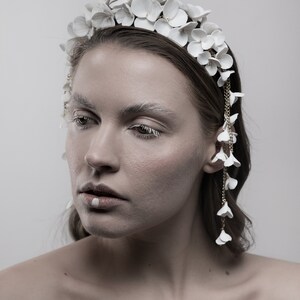 May include: A white flower headband with a delicate chain of white flowers dangling from the side. The headband is made of ceramic and has a simple, elegant design.
