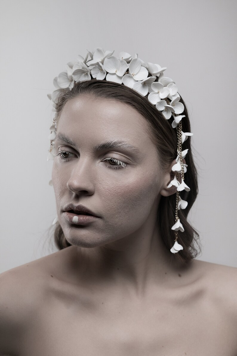 May include: A white flower headband with a delicate chain of white flowers dangling from the side. The headband is made of ceramic and has a simple, elegant design.