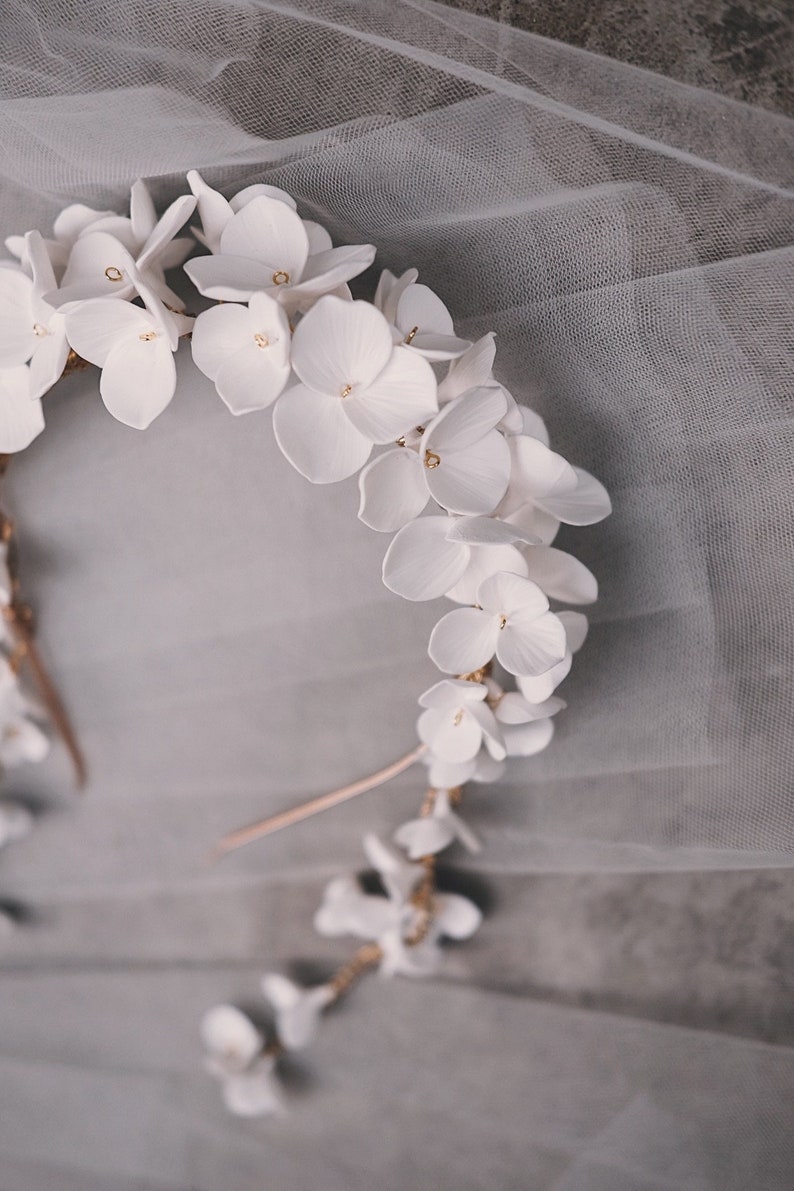 May include: A white floral crown with gold accents. The crown is made of delicate white flowers and is perfect for a wedding or special occasion.