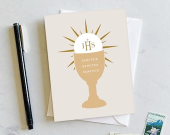 May include: A beige card with a gold chalice and host with the letters "IHS" and the words "Sanctus Sanctus Sanctus" printed on it.